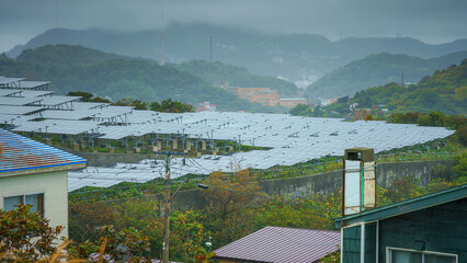Muroran, Hokkaido, Japan - Oct 4 2024, panoramic view of a solar power plant in a clearing, with mountains and houses covered in fog in background, without people, in cloudy weather, Muroran, Japan