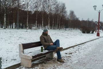 A young man is relaxing on a bench in a park. Spending time outdoors. A winter walk.