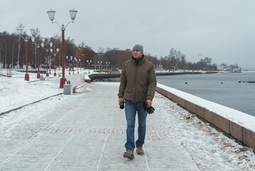 A young man walks along the city's embankment by the lake. The man enjoys a walk by the lake in winter.