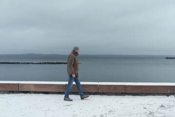 A man walks along the city embankment in winter. A winter daytime walk along the lake. Side view.