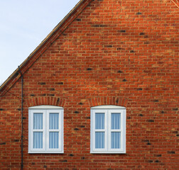 Residential building exterior showing red brick wall facade with two white framed windows under blue sky