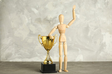 Wooden mannequin with gold cup on table near grunge wall