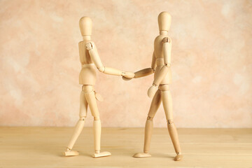 Wooden mannequins shaking hands on table near grunge wall