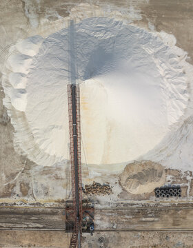 Aerial view of a stark, white salt pile contrasts against the earthy tones of the industrial landscape, Phuoc Diem, Ninh Thuan, Vietnam.