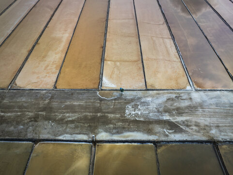 Aerial view of rectangular salt evaporation ponds displaying varying shades of brown and beige, reflecting the sky, Phuoc Diem, Ninh Thuan, Vietnam.