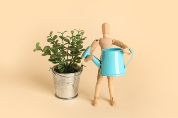 Wooden mannequin with watering can and plant on beige background