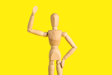 Wooden mannequin with raised hand on yellow background