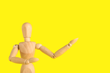 Wooden mannequin showing something on yellow background