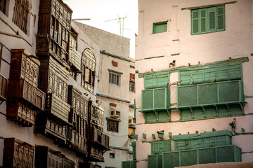 View of the contrasting dark wood and pastel pink buildings with ornate green shutters and balconies, Jeddah, Saudi Arabia.