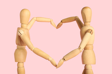 Wooden mannequins making heart gesture on pink background