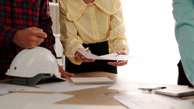 Architect and safety engineer discussion about building blueprint displaying on laptop on table with architectural document and wooden block scatter around at modern office. Closeup. Delineation.