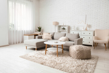 Interior of light living room with table, pouf and sofa near white brick wall