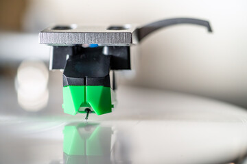 Turntable cartridge with stylus needle touching vinyl record, analog audio nostalgia. Close up macro photo.