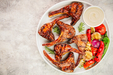 Middle Eastern traditional dish with grilled juicy lamb chops/ribs placed with grilled veggies and tahini sauce. Top view with copy space.