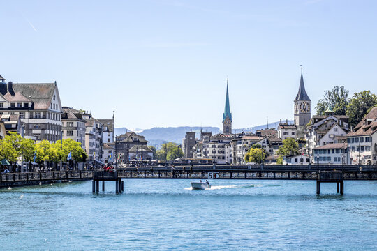 View of the serene turquoise river reflecting the bright sky, with a bridge connecting the quaint European buildings in Zurich, Switzerland.
