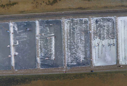 Aerial view of salt evaporation ponds reflecting the sky, creating a mosaic of textures and tones, with workers harvesting salt, Long Dien, Ba Rịa - Vung Tau, Vietnam.