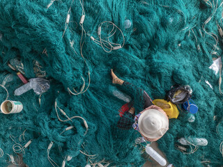 Aerial view of a woman amidst a sea of vibrant turquoise fishing nets, her conical hat a stark contrast against the tangled web, Thuan An, Bình Duong, Vietnam.