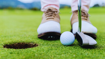Golfer preparing to putt ball near hole.