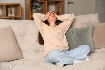 Young woman sitting on sofa and suffering from headache at home