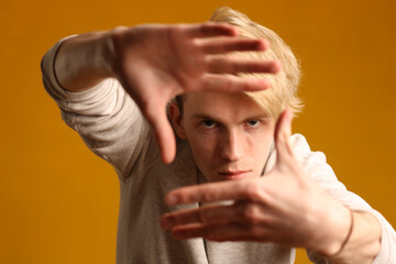 A cute teenager spreads his arms in front of him while posing against a yellow background during a photo shoot.