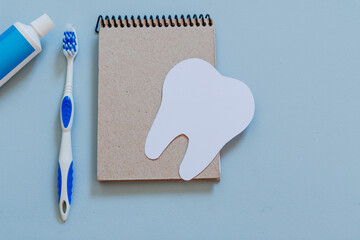 Paper tooth on a notebook, next to a toothbrush and toothpaste, copy space. Design for dentist's day greeting card.