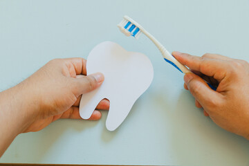 Hand holding a cardboard tooth and a toothbrush, blue background
