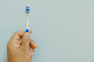 Hand holding a toothbrush, light blue background, copy space