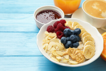Healthy breakfast. Oatmeal with nuts, banana, berries, jam, coffee and juice on light blue wooden table, closeup. Space for text