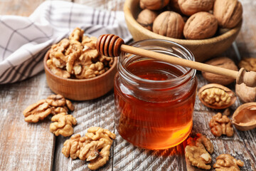 Honey in jar, walnuts and dipper on wooden table, closeup
