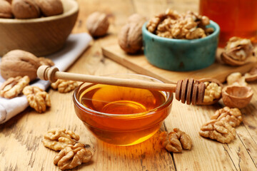 Delicious honey in glass bowl, dipper and walnuts on wooden table, closeup