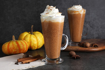 Delicious pumpkin latte with whipped cream, spices and fresh vegetables on dark textured table, closeup