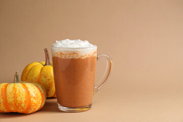 Delicious pumpkin latte with whipped cream in glass cup and fresh vegetables on beige background, closeup. Space for text