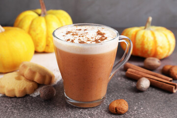 Delicious pumpkin latte in glass cup, spices, cookies and fresh vegetables on grey textured table, closeup