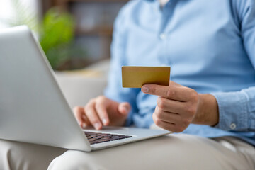 Man holding a blank gold credit card while inputting payment details on a silver laptop, representing secure online banking, e-commerce transactions, and digital finance
