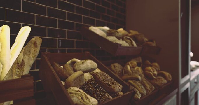 Warm, crusty loaves of bread are arranged on wooden shelves. The bakery has a welcoming atmosphere, with a dark tiled wall that complements the baked goods.