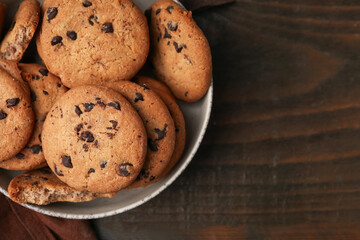 Yummy chocolate chip cookies in bowl on wooden table, top view. Space for text