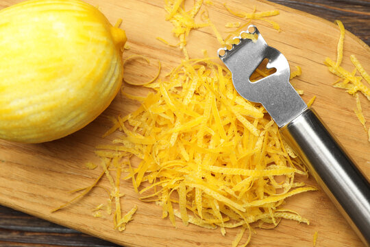 Lemon zest, fresh fruit and zester tool on wooden table, top view
