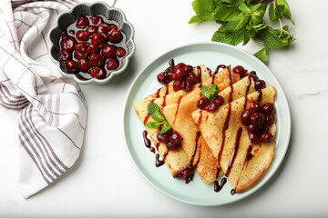 Delicious crepes served with cherry jam and chocolate on white marble table, flat lay