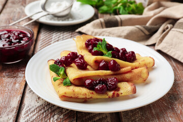 Tasty crepes with cherries and mint served on wooden table, closeup