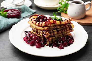 Tasty crepes with cherries, chocolate and mint served on black table, closeup