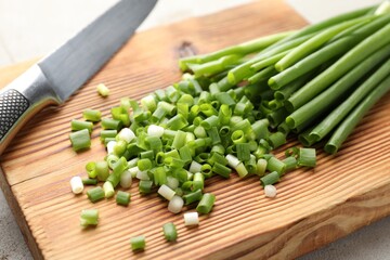 Cut green onions and knife on light grey table, closeup