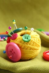 Bright yarn with pins and buttons on light green cloth, closeup