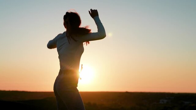 Young smiling woman dancing against sky outdoors. Holiday party. Beautiful girl dancing and having fun with friends at sunset disco. Cheerful woman moving her hands to music at party. Party on beach