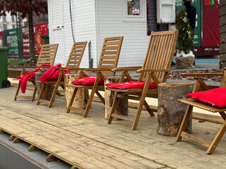 Wooden lounge chairs with red blankets near an outdoor winter ice rink. Cozy rest area, seasonal comfort, and festive urban leisure