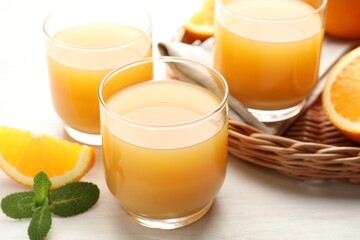 Fresh orange juice, mint and fruits on light wooden table, closeup