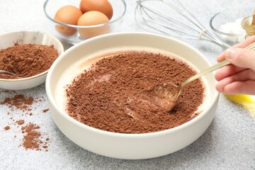 Woman stirring cocoa powder with dough at grey textured table, closeup