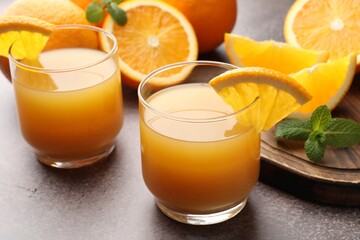 Fresh orange juice in glasses, mint and fruits on grey table, closeup