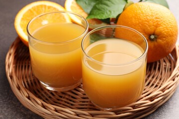 Fresh orange juice, fruits and green leaves on grey table, closeup