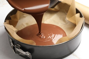 Pouring liquid chocolate dough into baking dish at white marble table, closeup