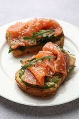 Tasty bruschettas with salmon, arugula and avocado on light grey table, closeup